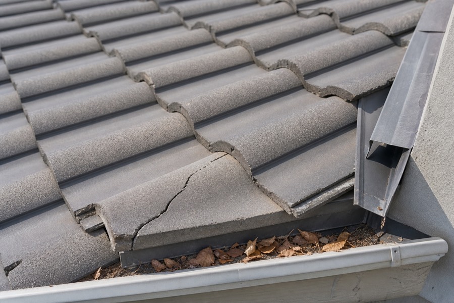 Cracked roof tile, loose flashing, and leaves near a gutter showing common roof maintenance warning signs